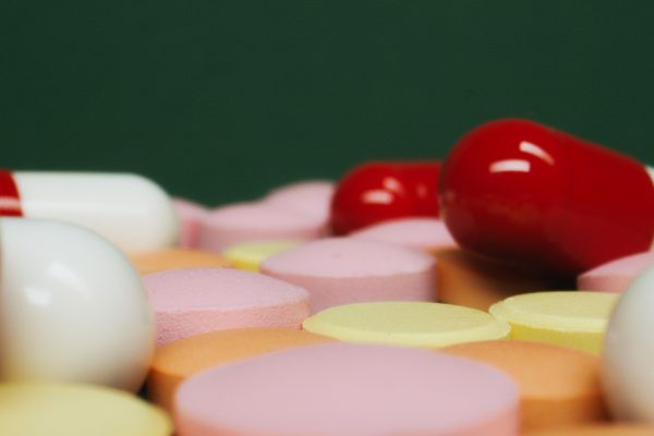 A close-up view of various colorful pills and tablets on a green background, focusing on medication variety. Une vue rapprochée de diverses pilules et comprimés colorés sur un fond vert, mettant l'accent sur la variété des médicaments.
