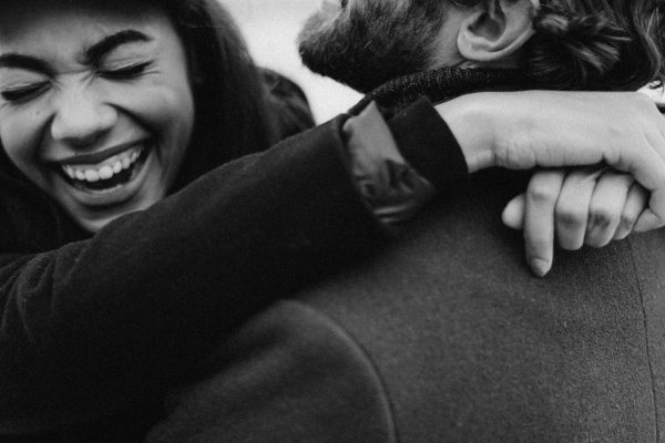 Black and white image of a joyful couple embracing and laughing, capturing a loving moment. Image en noir et blanc d'un couple joyeux s'embrassant et riant, capturant un moment d'amour.
