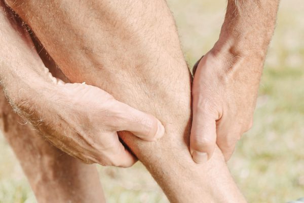 A man outdoors massaging his calf, dealing with muscle pain during sports activities. Un homme en extérieur se massant le mollet, souffrant de douleurs musculaires pendant les activités sportives.
