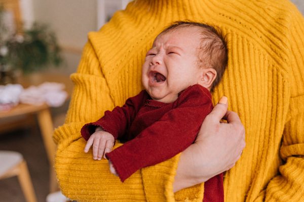 Emotional portrait of a crying newborn being comforted in caregiver's arms indoors. Portrait émotionnel d'un nouveau-né en pleurs réconforté dans les bras d'un soignant à l'intérieur.