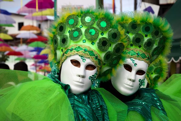 Scène de carnaval colorée avec des masques et des parapluies suspendus créant une atmosphère festive.