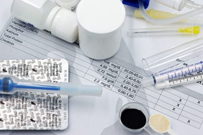 Vet supplies like syringes and medicines on blood test reports, suggesting medical care theme. Fournitures vétérinaires comme les seringues et les médicaments sur les rapports de tests sanguins, suggérant un thème de soins médicaux.