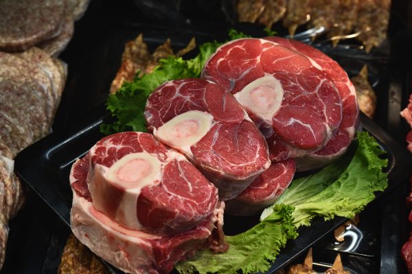 Close-up of fresh raw osso buco on display with green lettuce leaves. Gros plan d'osso buco cru frais exposé avec des feuilles de laitue verte.