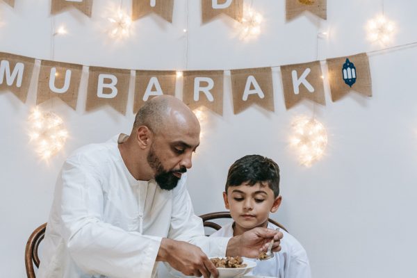 Father and son enjoying a festive Eid meal together indoors, creating cherished family moments. Un père et son fils savourant un repas festif d'Eid ensemble à l'intérieur, créant des moments familiaux précieux.