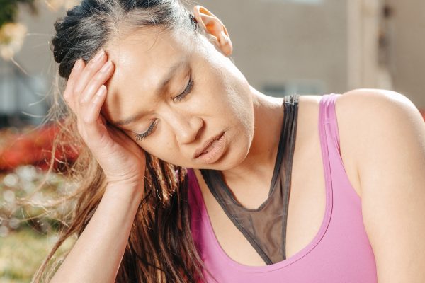 A woman in a purple top experiencing a headache under bright sunlight. Une femme en haut violet souffrant d'une migraine sous un soleil intense.