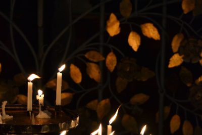 Candles burn softly on a metal stand against a metal fence backdrop in Germany. Les bougies brûlent doucement sur un support métallique devant un fond de clôture métallique en Allemagne.